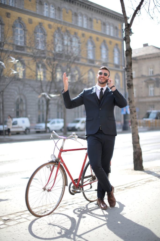 man in black suit jacket and black pants standing beside red bicycle